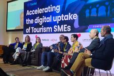 8 people sitting in front of a screen, having a discussion. In the background there is a screen with the text Accelerating the digital uptake of Tourism SMEs