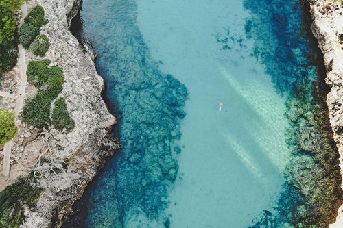 a wide emerald river from above, rocky shore, a person swimming in the river