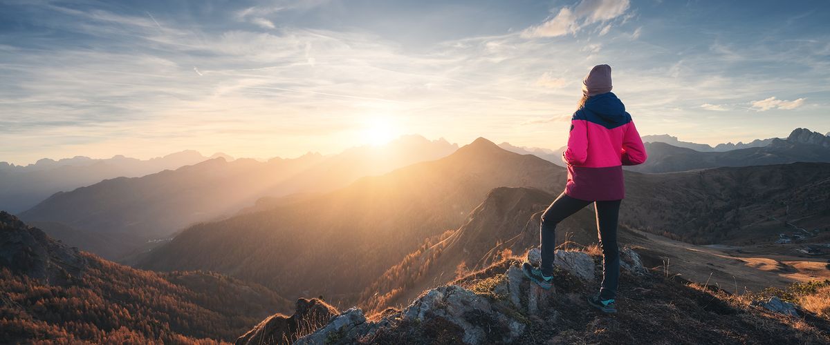 Woman standing at the top of a mountain and looking at the sunset 