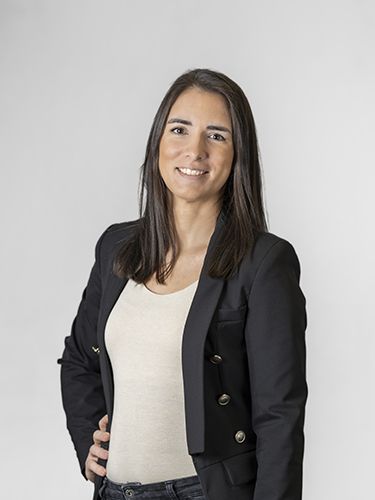 A portrait of Ana Furlani, HR manager. She is a middle-aged woman with long brown hair, wearing a white shirt and a black jacket, smiling.